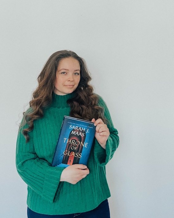 Zenia Radoor holding the book ‘Throne of Glass’ by Sarah J. Maas, used in the ‘Explore the Blog’ section to highlight categories like books, writing, and self-care.